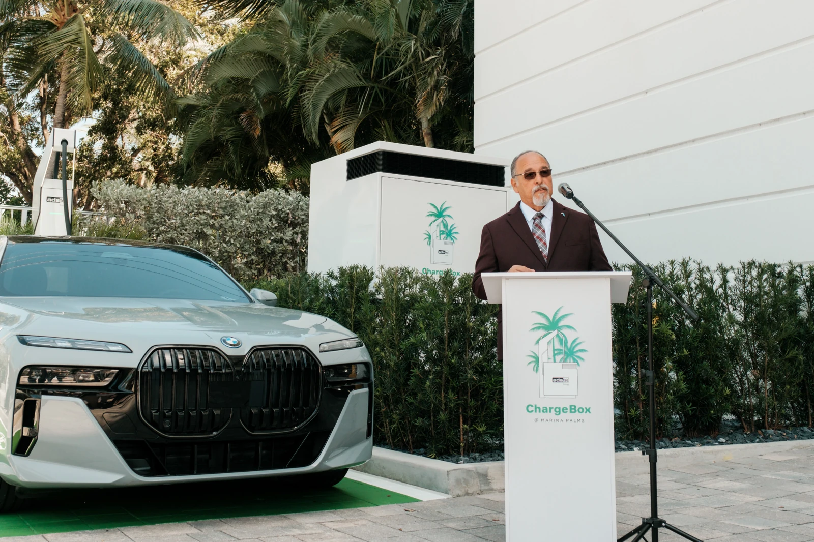 George Barriere at the Marina Palms EV-charging launch, with the charging dispenser, vehicle, battery cabinet, and podium visible